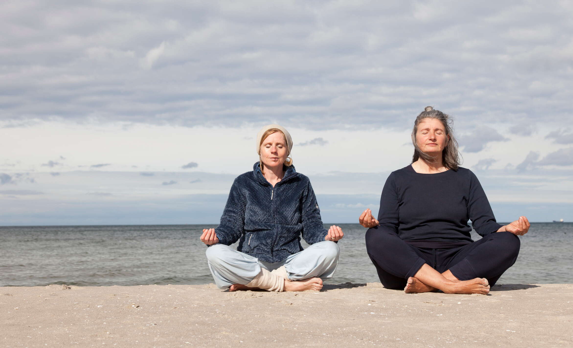 Anne Rosinski mit Teilnehmerin machen Atemübungen am Strand vor dem Meer