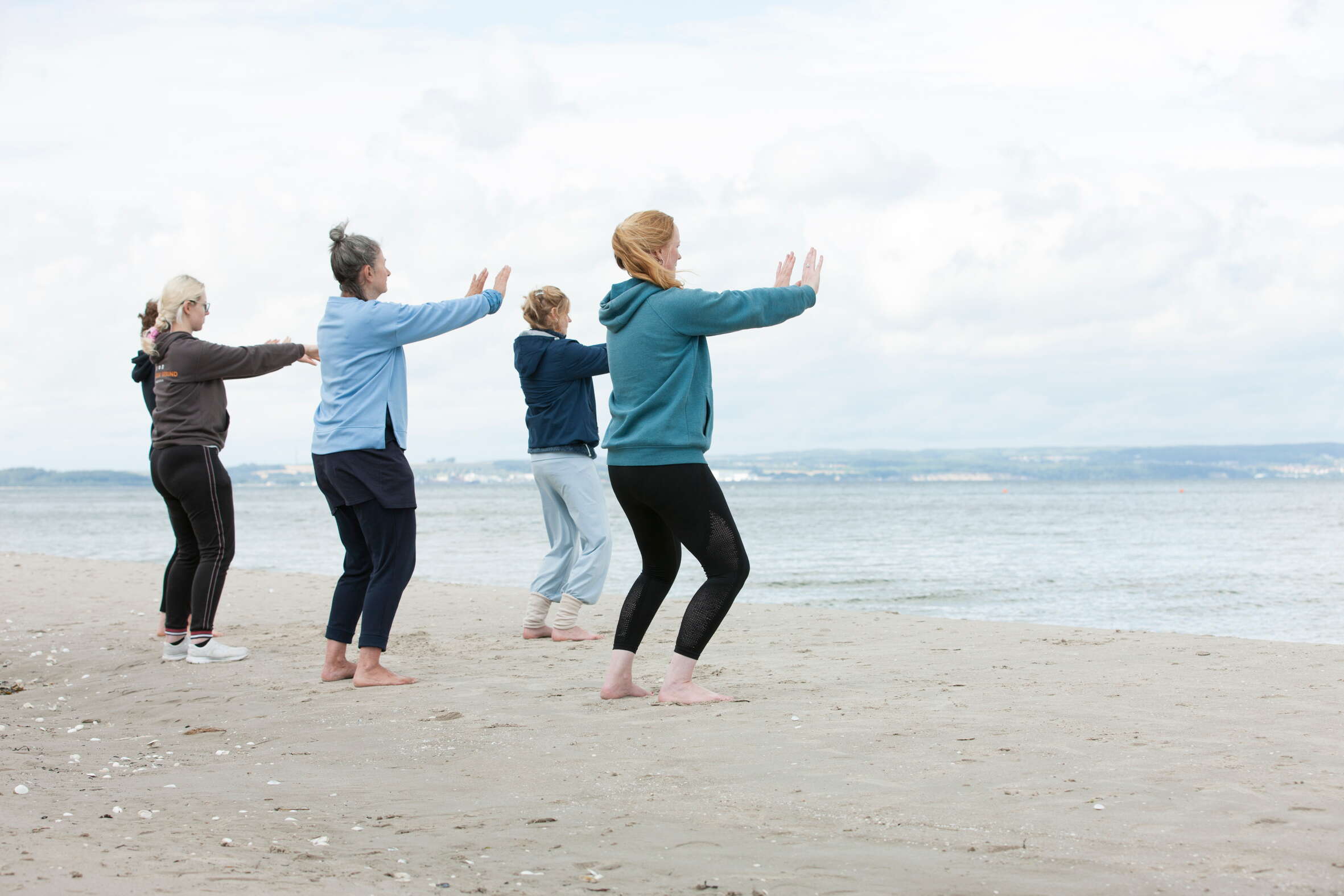 Eine Gruppe von Frauen macht Yoga am Strand, im Hintergrund das Meer